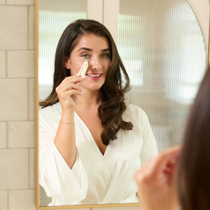Woman applying eye serum to her face in front of a mirror