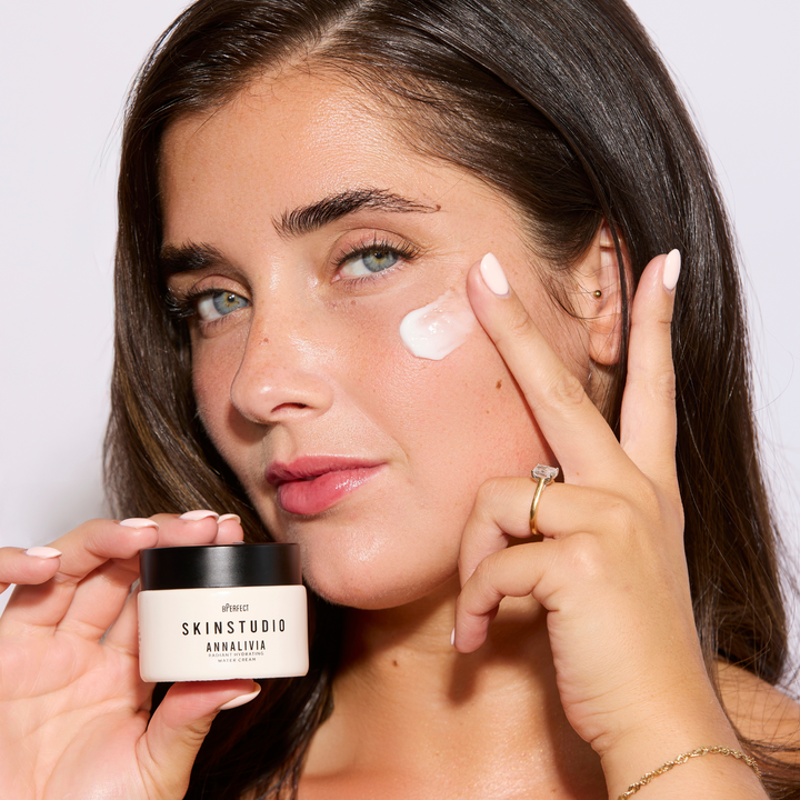 Woman applying cream to her face with a jar of Skin Studio product.