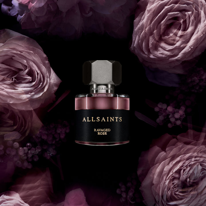 Allsaints Ravaged Rose perfume bottle surrounded by purple flowers on a dark background