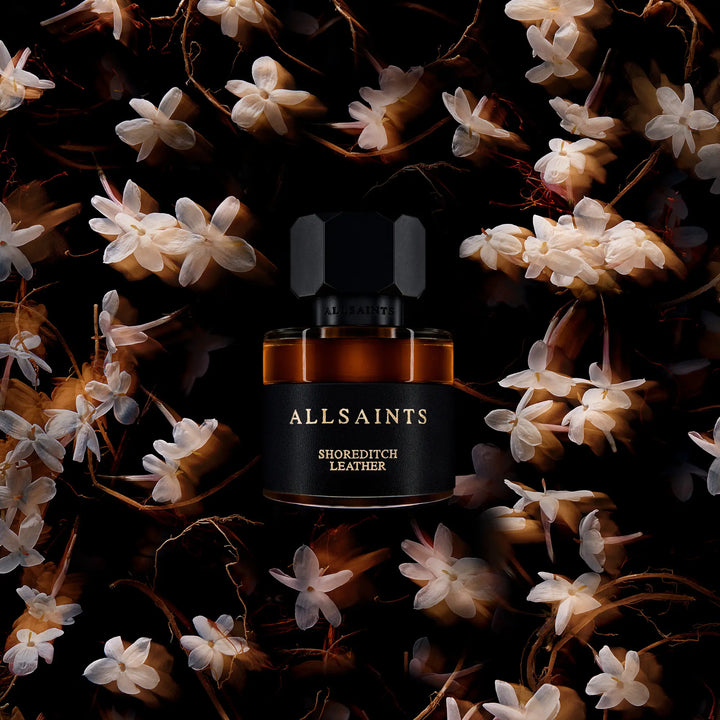 AllSaints Shoreditch Leather perfume bottle surrounded by flowers on a dark background
