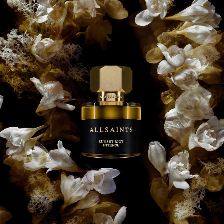 AllSaints perfume bottle surrounded by flowers on a dark background