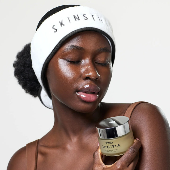 Woman wearing a 'SKINSTUDIO' headband holding a jar of skincare product.