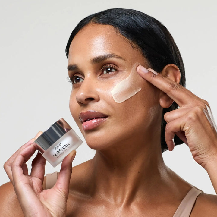 Woman applying skincare cream to her face with a jar of the product in hand.