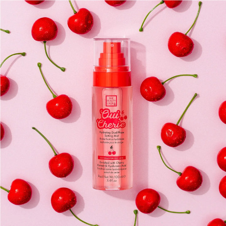 The beauty crop oui cherie hydrating dual-phase setting mist red bottle with red spray cap on a lilac background with cherry decorations