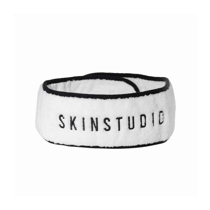 A white microfiber skincare headband with the text 'SKINSTUDIO' printed in black.