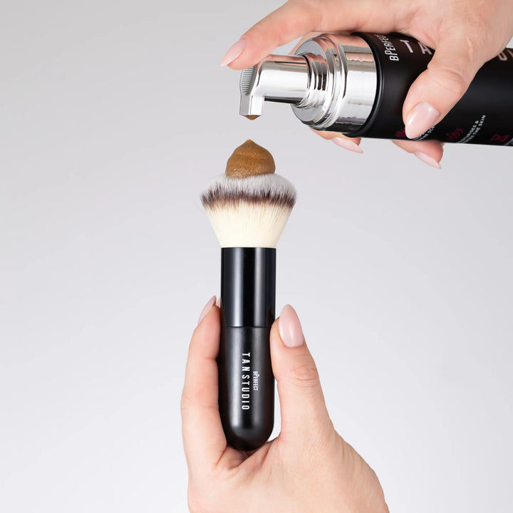 Makeup brush with a black handle being filled with mousse from a container.