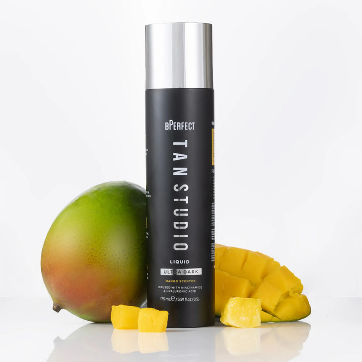 BPerfect Tan Studio liquid bottle with mangoes on a white background